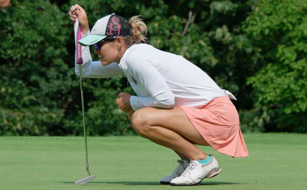 female golfer in white top and light peach shorts holding a putter