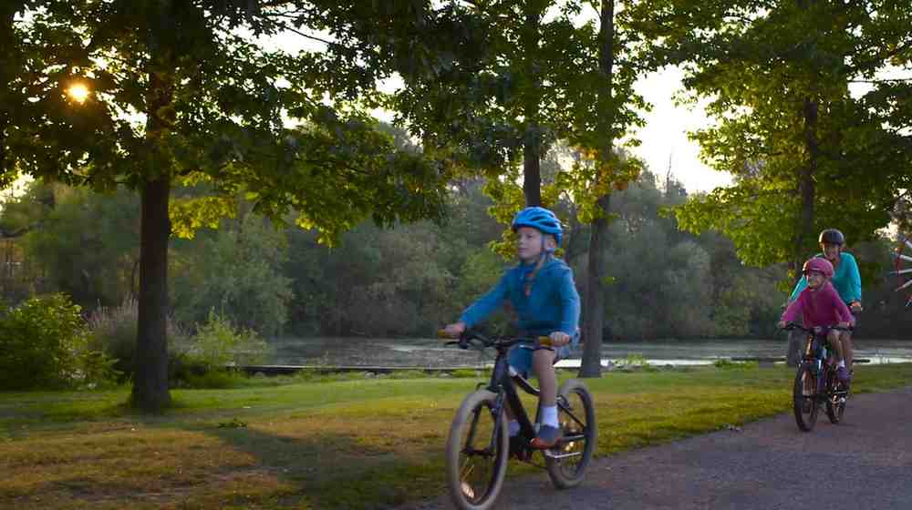 family riding a bike trail in a wooded area next to a river